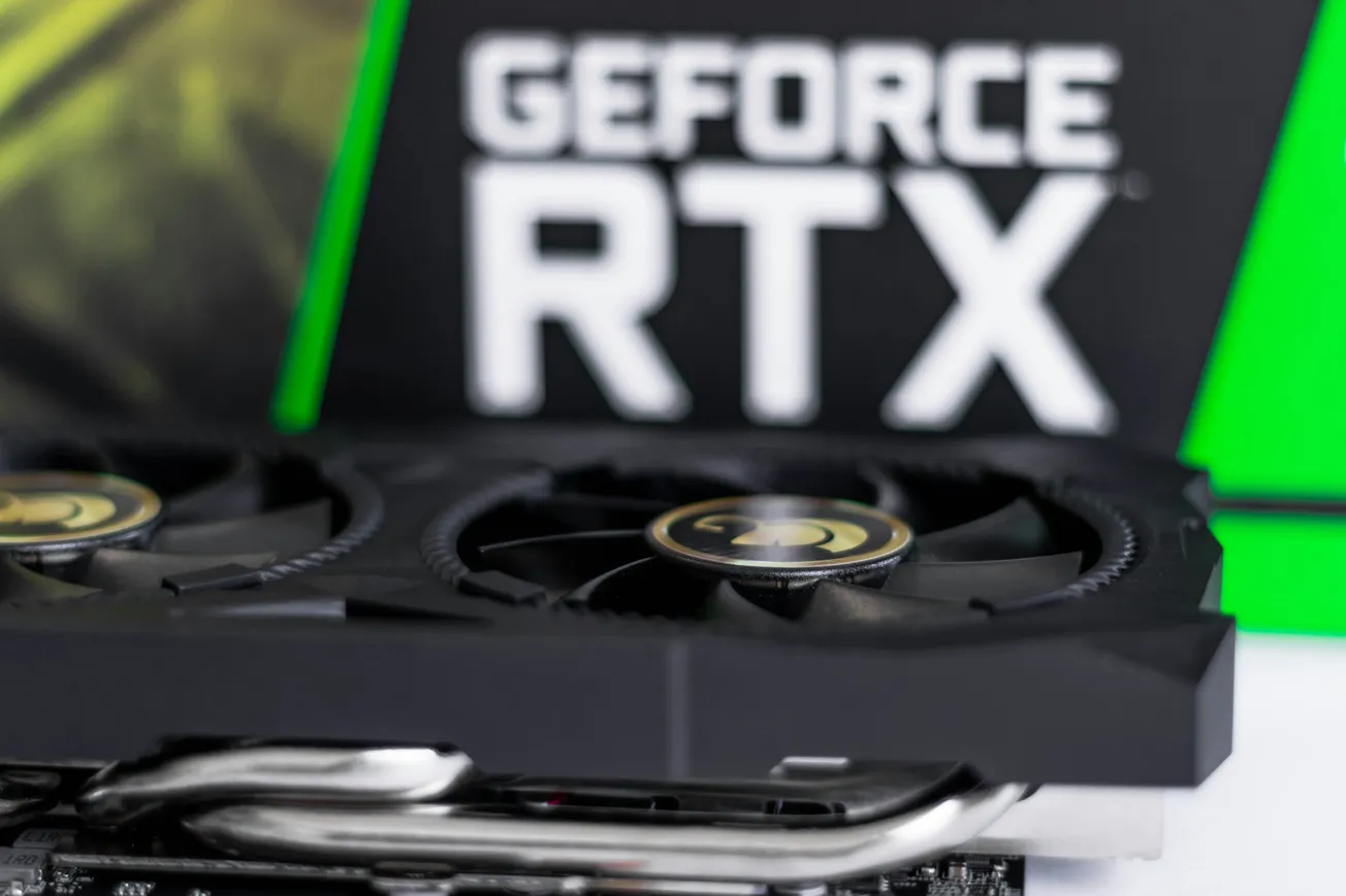 Close-up of an NVIDIA GeForce RTX graphics card, featuring dual fans and sleek design. Background shows a blurred green and black RTX logo.