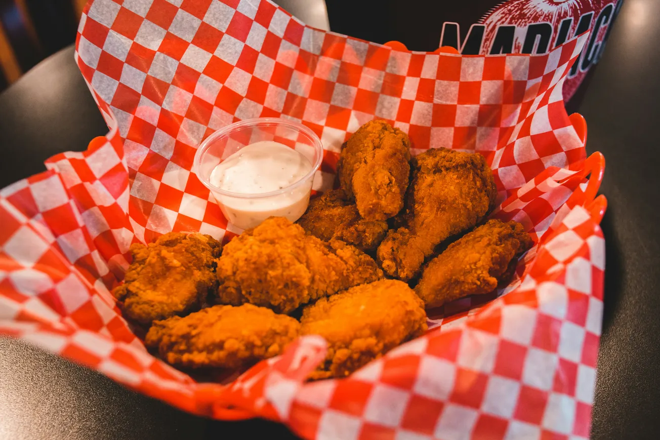 Basket of crispy fried chicken wings on red checkered paper, with a side of creamy dipping sauce. Warm, inviting, and deliciously appetizing.
