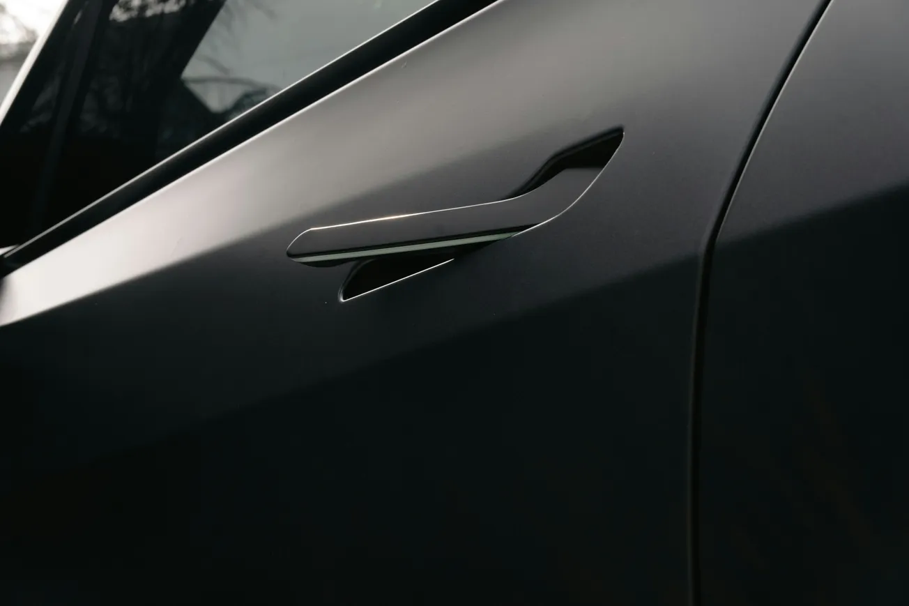 Close-up of a sleek, black car door with a modern, flush handle design. The matte finish and smooth lines convey a sense of elegance and innovation.