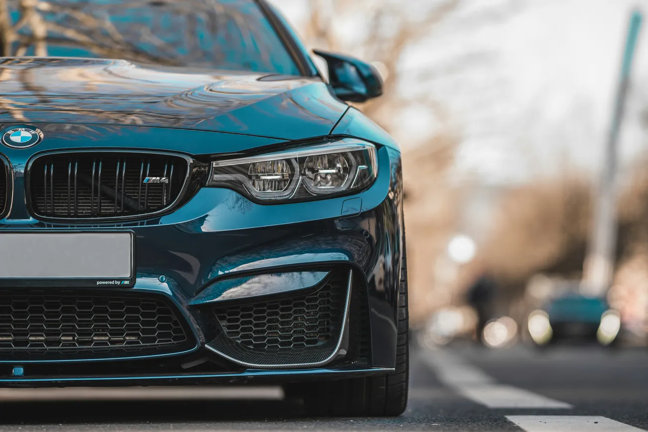 Close-up view of a sleek blue BMW car on a street, showing the front grille and headlights. The background is blurred, conveying a dynamic urban scene.