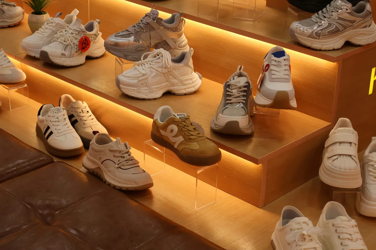 Display of various sneakers on illuminated wooden shelves, showcasing different styles and colors. The warm lighting gives a cozy, inviting ambiance.