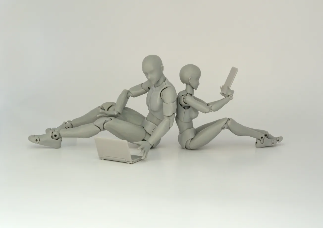 Two gray humanoid figurines sit back-to-back. One uses a laptop, the other holds a smartphone, conveying a theme of technology and communication.