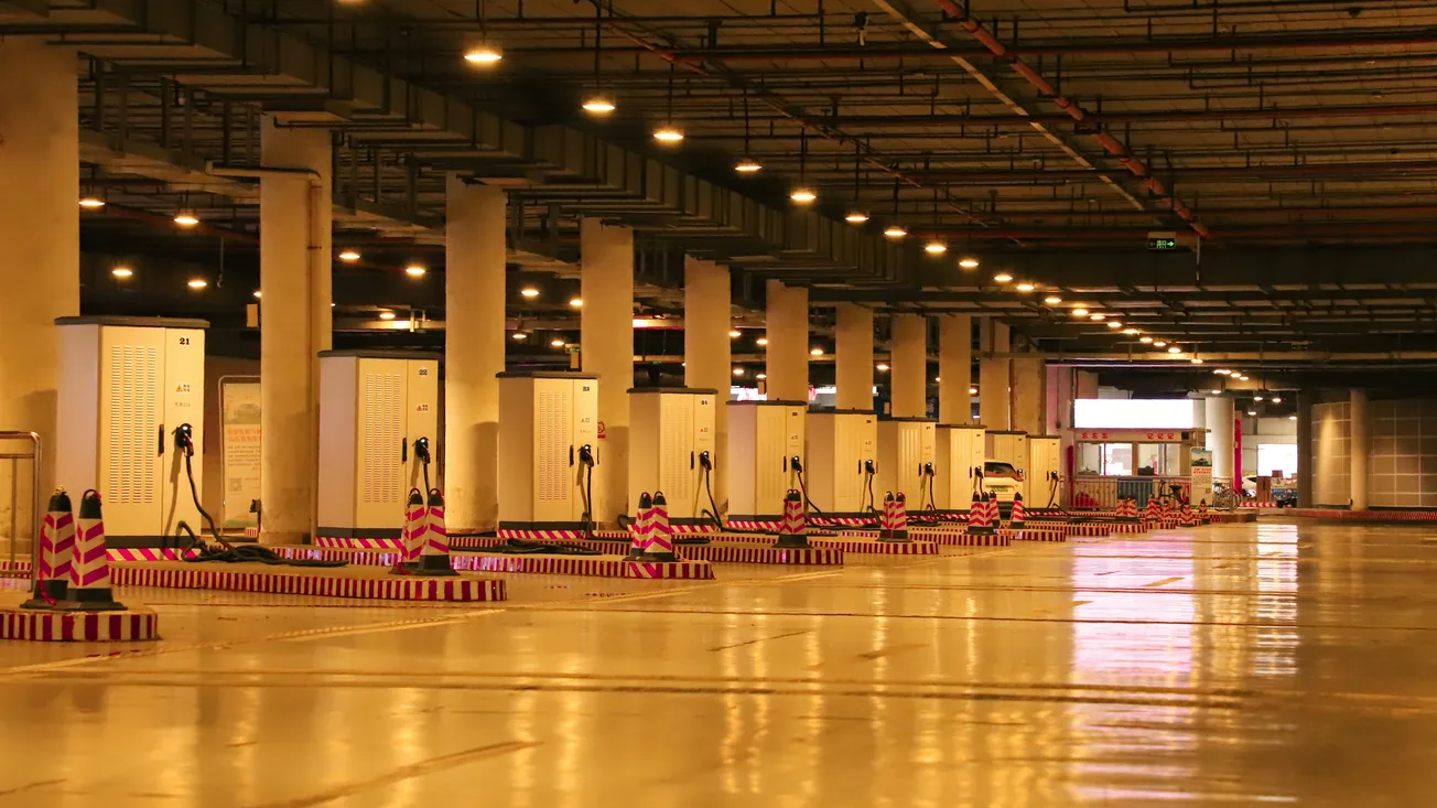 A modern, spacious underground parking garage with bright lighting and marked electric charging stations. The shiny floor and neat arrangement convey order.