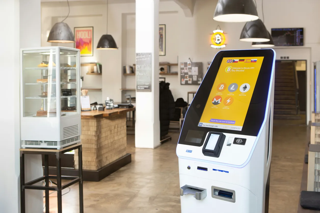 A modern café interior featuring a Bitcoin ATM in the foreground. The café has cozy lighting, a pastry display, and rustic décor, creating a tech-meets-comfort vibe.