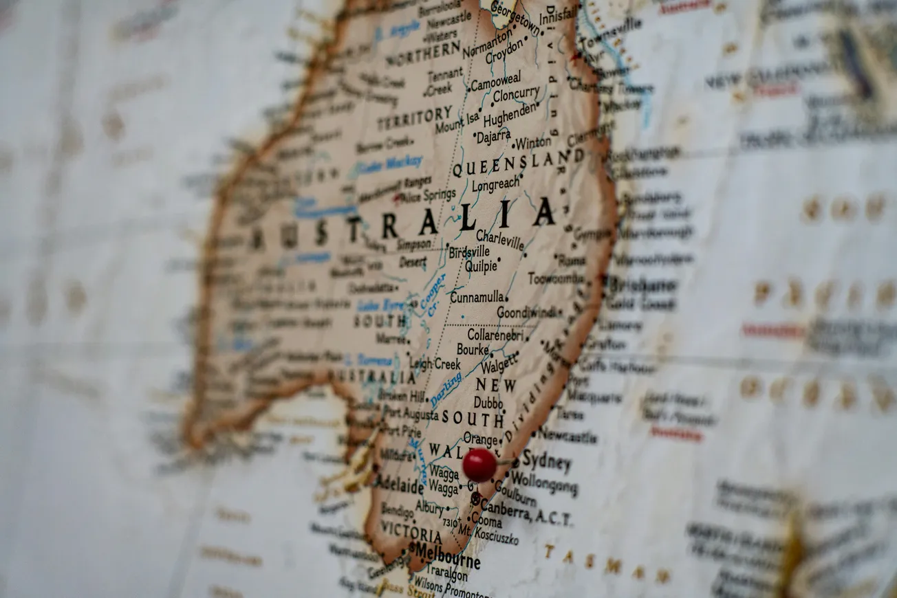 A close-up map of Australia highlights major cities and regions. A red pin marks Canberra, conveying a sense of travel or focus on the city.