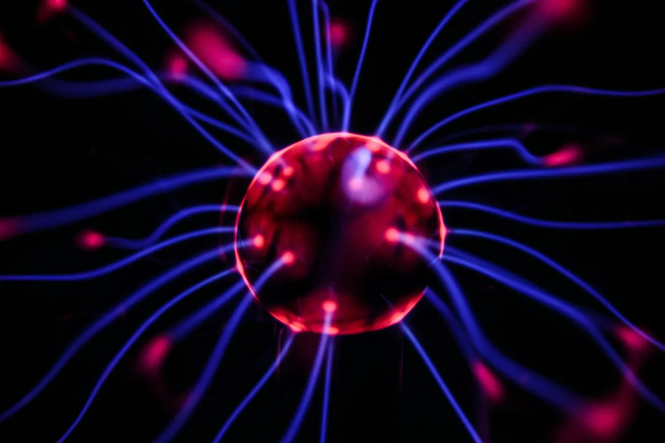 A vibrant plasma globe emits glowing blue and pink strands of light from a central sphere against a dark background, creating an energetic and dynamic effect.