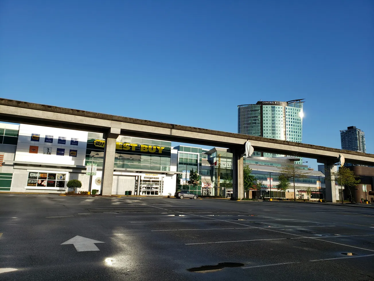 A modern retail shopping center exterior with customer parking areas under a clear sky.