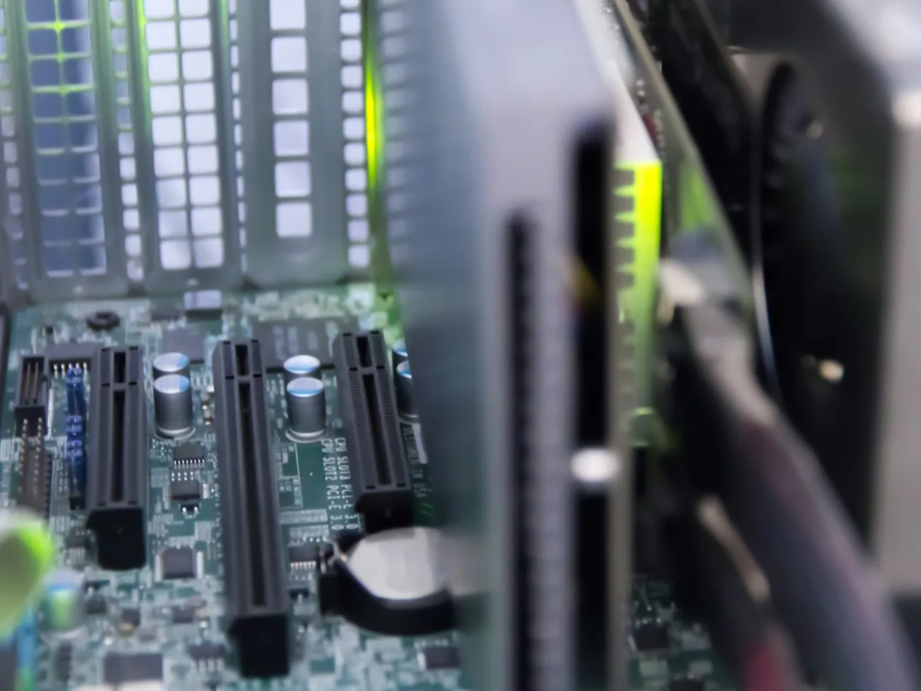 Close-up of a computer motherboard showing PCI slots, capacitors, and circuit paths. Soft green light hints at a powered-on state, conveying a tech-focused atmosphere.