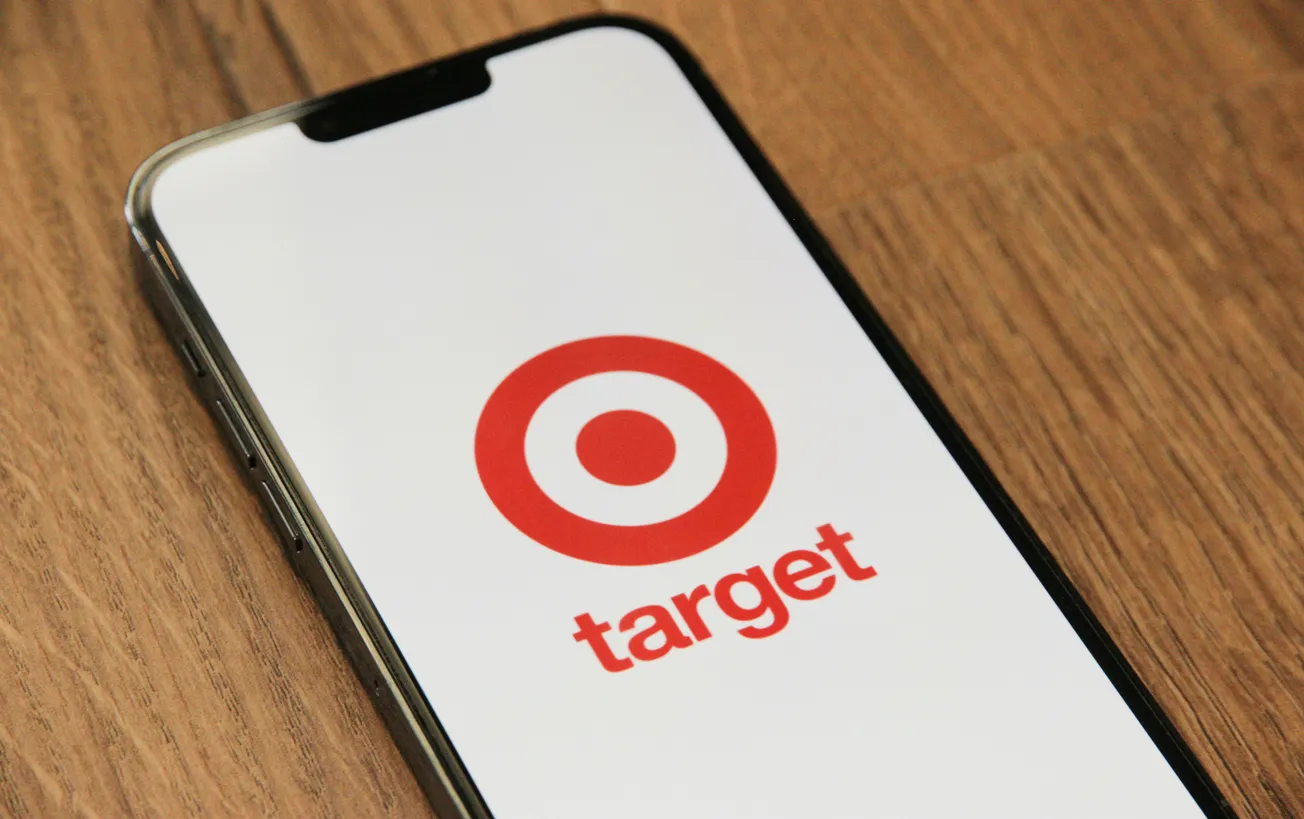 Smartphone on a wooden surface displays the Target logo, featuring a red bullseye and the word "target" in red, conveying a clean, modern look.