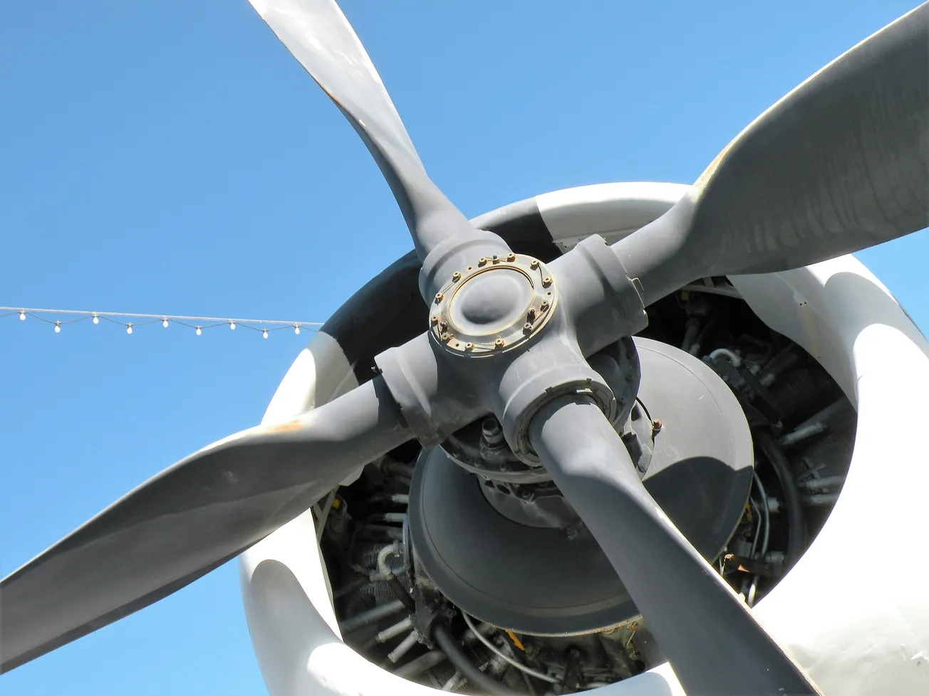 Close-up of a vintage aircraft propeller with four blades against a clear blue sky, conveying a sense of aviation history and engineering.