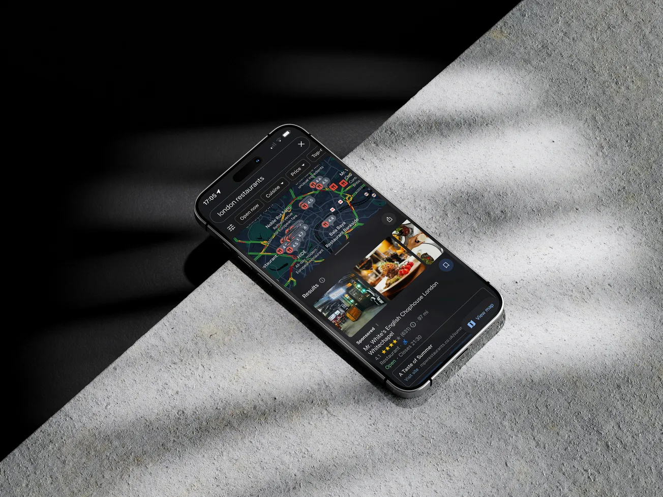 A smartphone displaying a dark-themed map app with location pins lies on a shaded, textured surface. The mood is sleek and modern, suggesting travel or navigation.