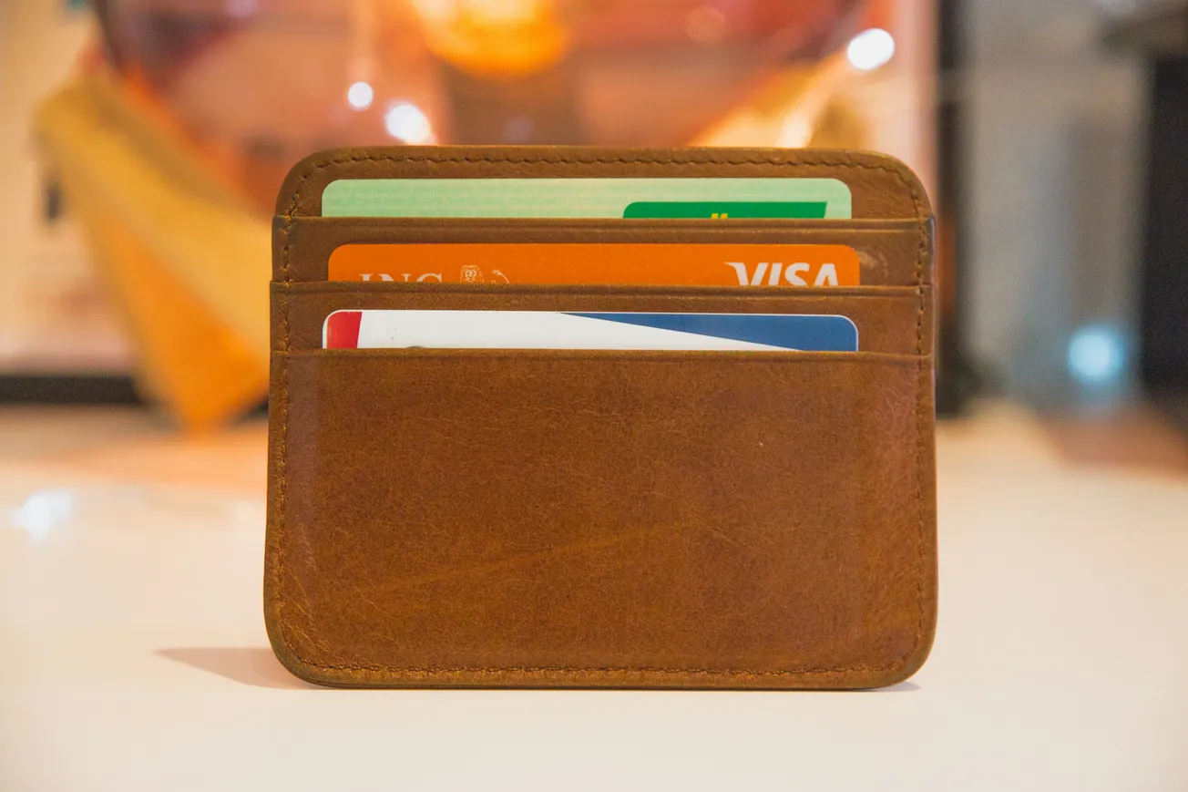 Close-up of a brown leather card wallet holding several credit and ID cards. The background is softly blurred, providing a warm, cozy ambiance.