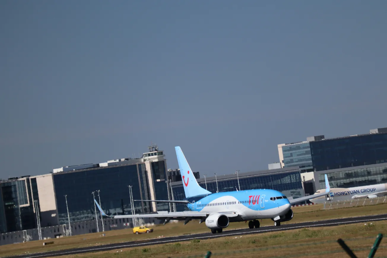 A blue and white airplane taxis on a runway at an airport, with modern glass buildings in the background under a clear blue sky.