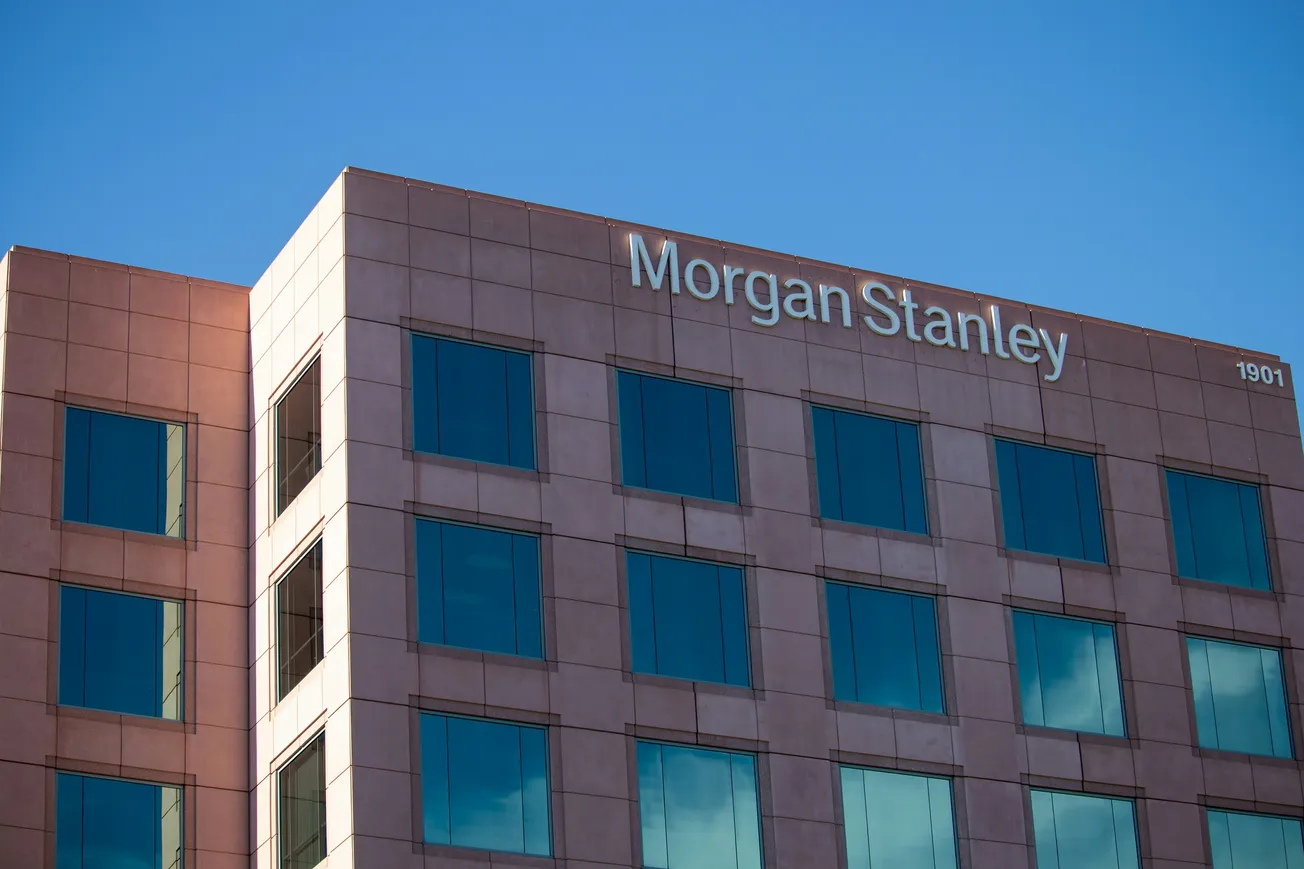 A brown office building with the name "Morgan Stanley" at the top, reflecting a clear blue sky in its windows, suggesting corporate professionalism.